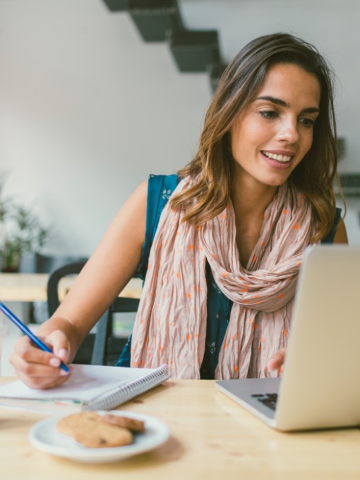 woman writing in notebook and looking at laptop screen